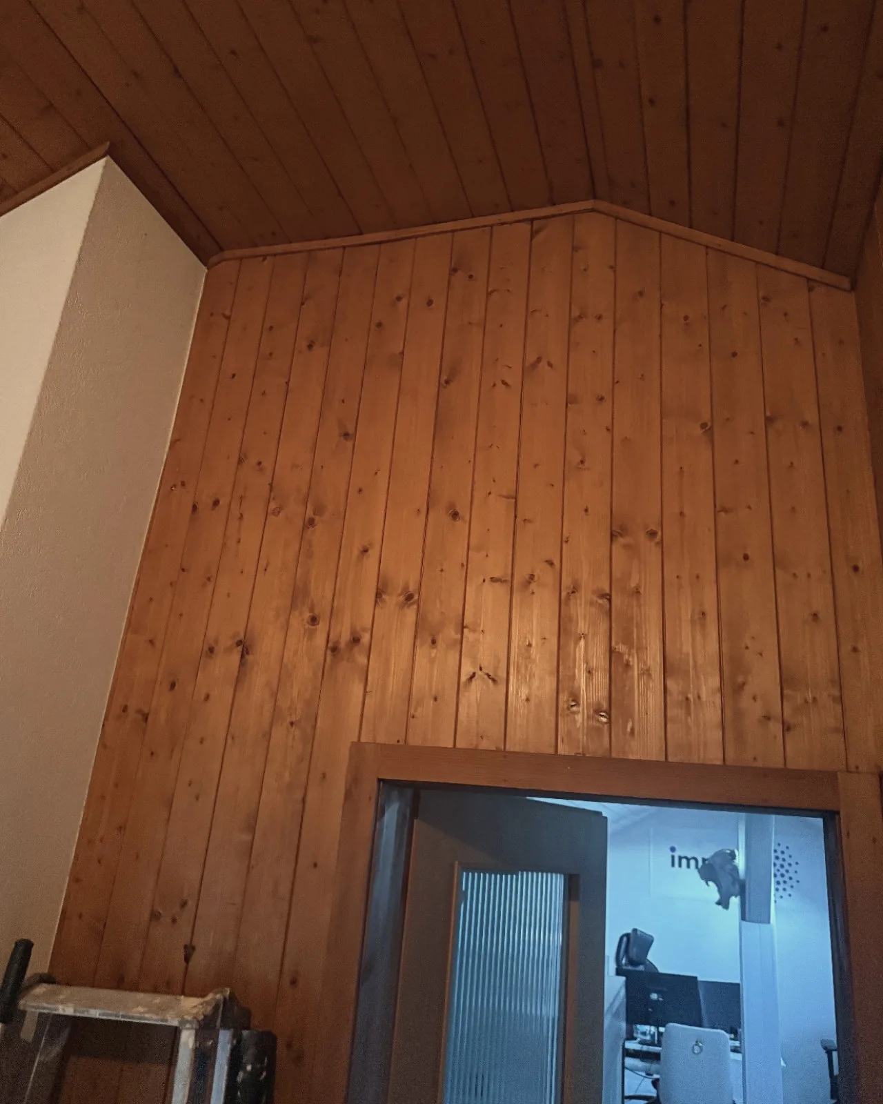 Pignon en lambris de sapin orangé au-dessus d’une porte vitrée, avant les travaux